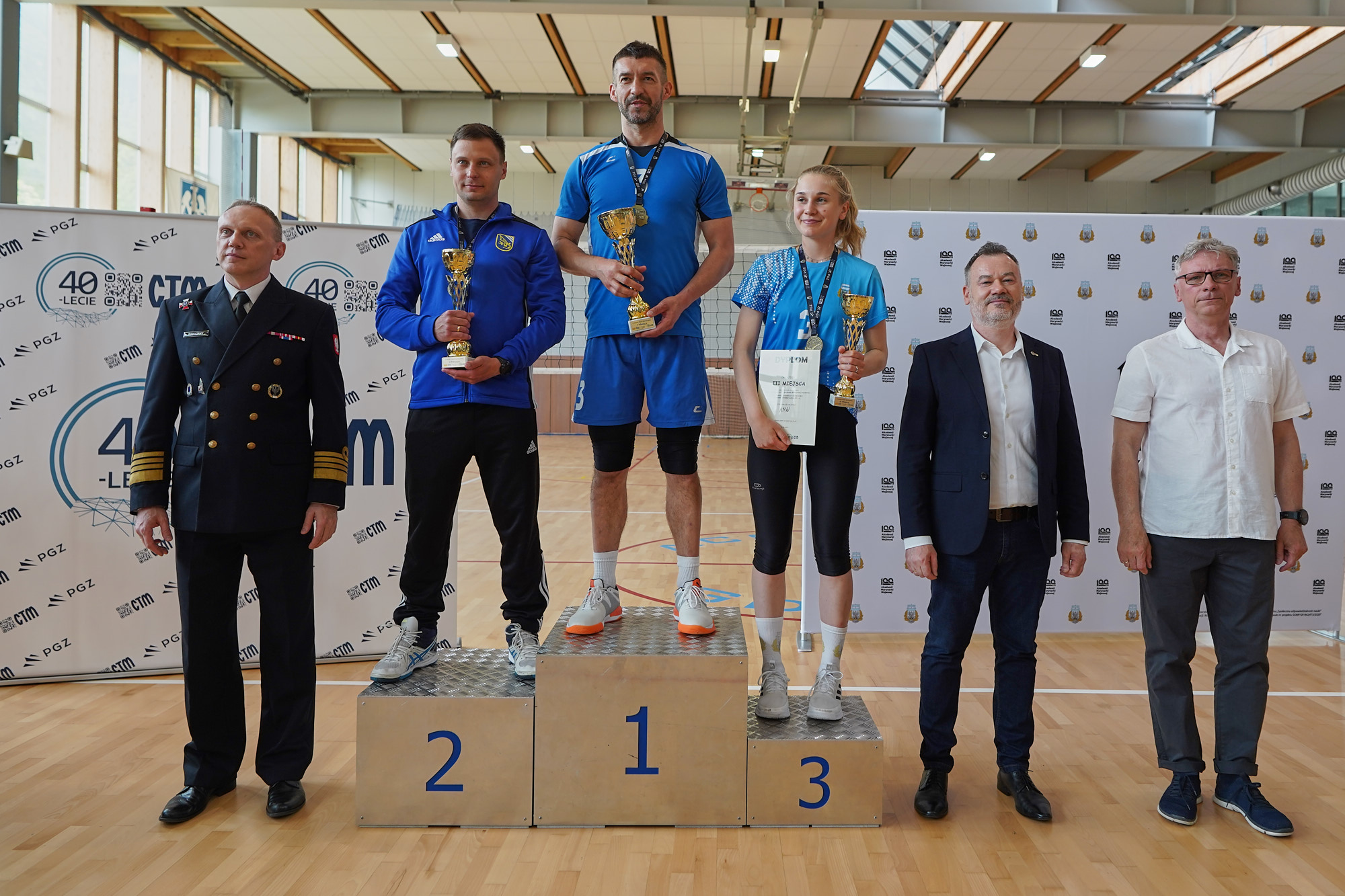 Zwycięzcy turnieju na podium z pucharami — oficer Marynarki Wojennej i przedstawiciele CTM przy banerach jubileuszowych