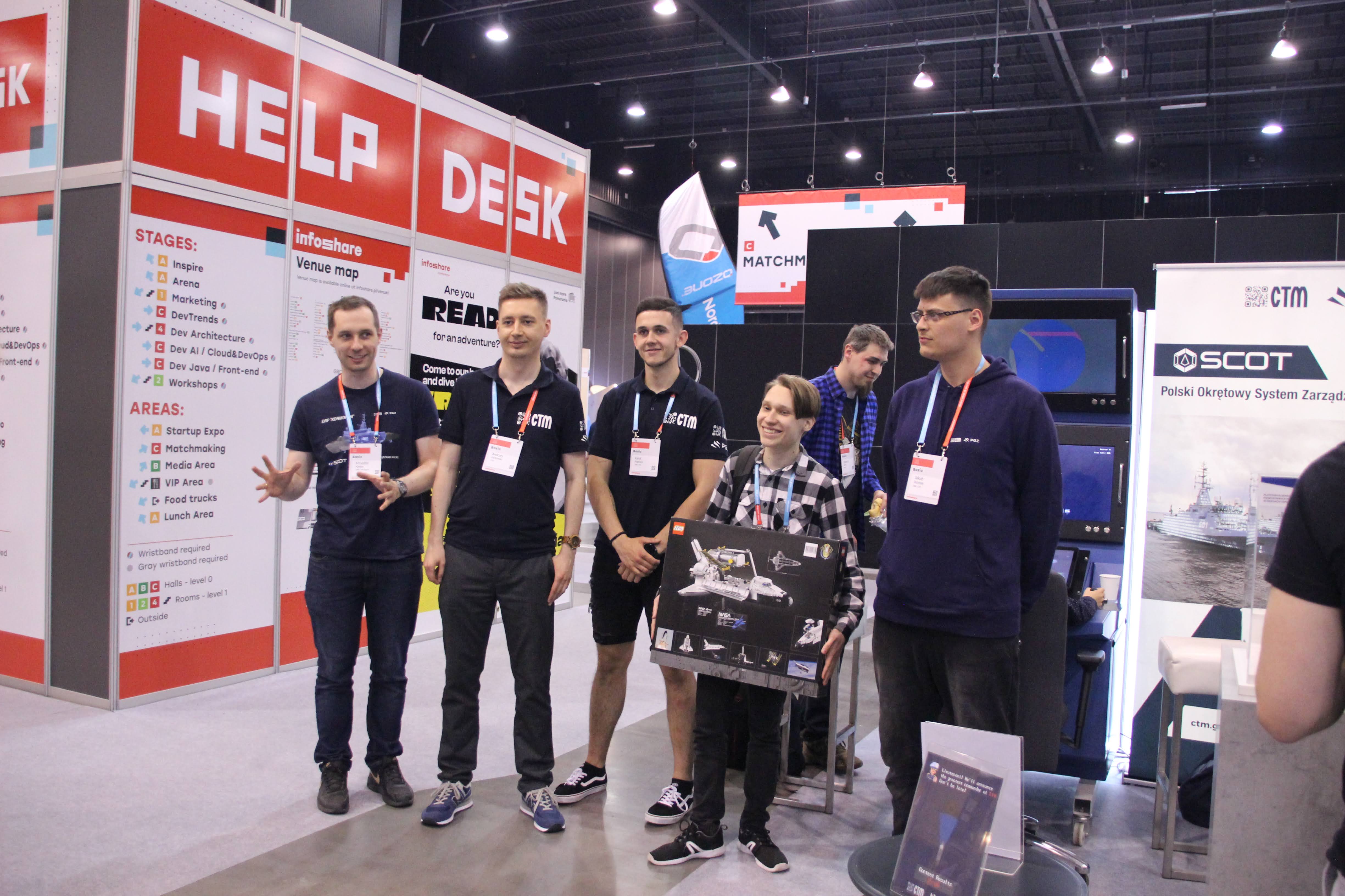 Pracownicy CTM ze zwycięzcą konkursu trzymającym zestaw LEGO — baner SCOT i napis Help Desk w tle