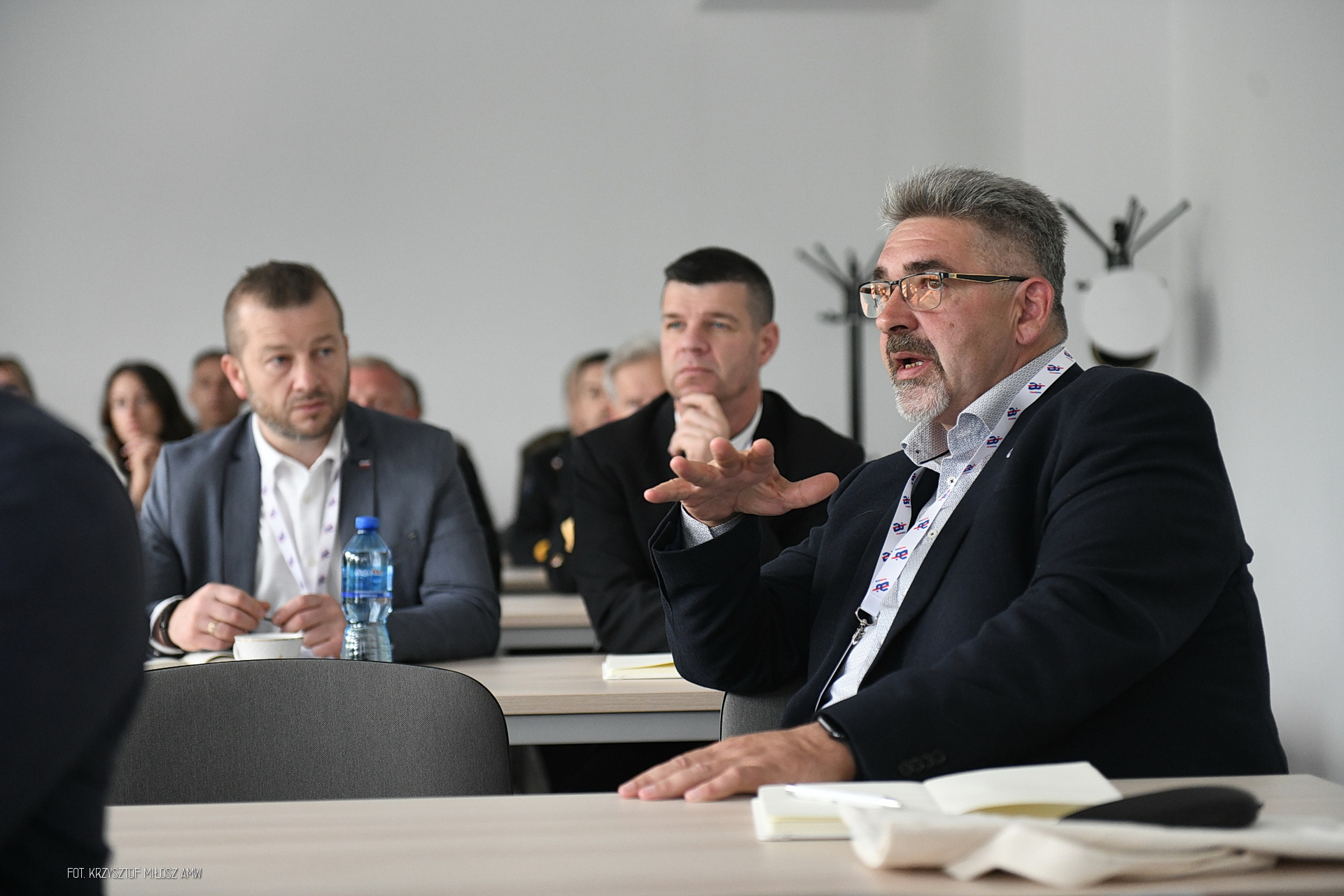 Uczestnik konferencji Digital Baltic gestykuluje podczas dyskusji przy stole — w tle słuchacze w garniturach