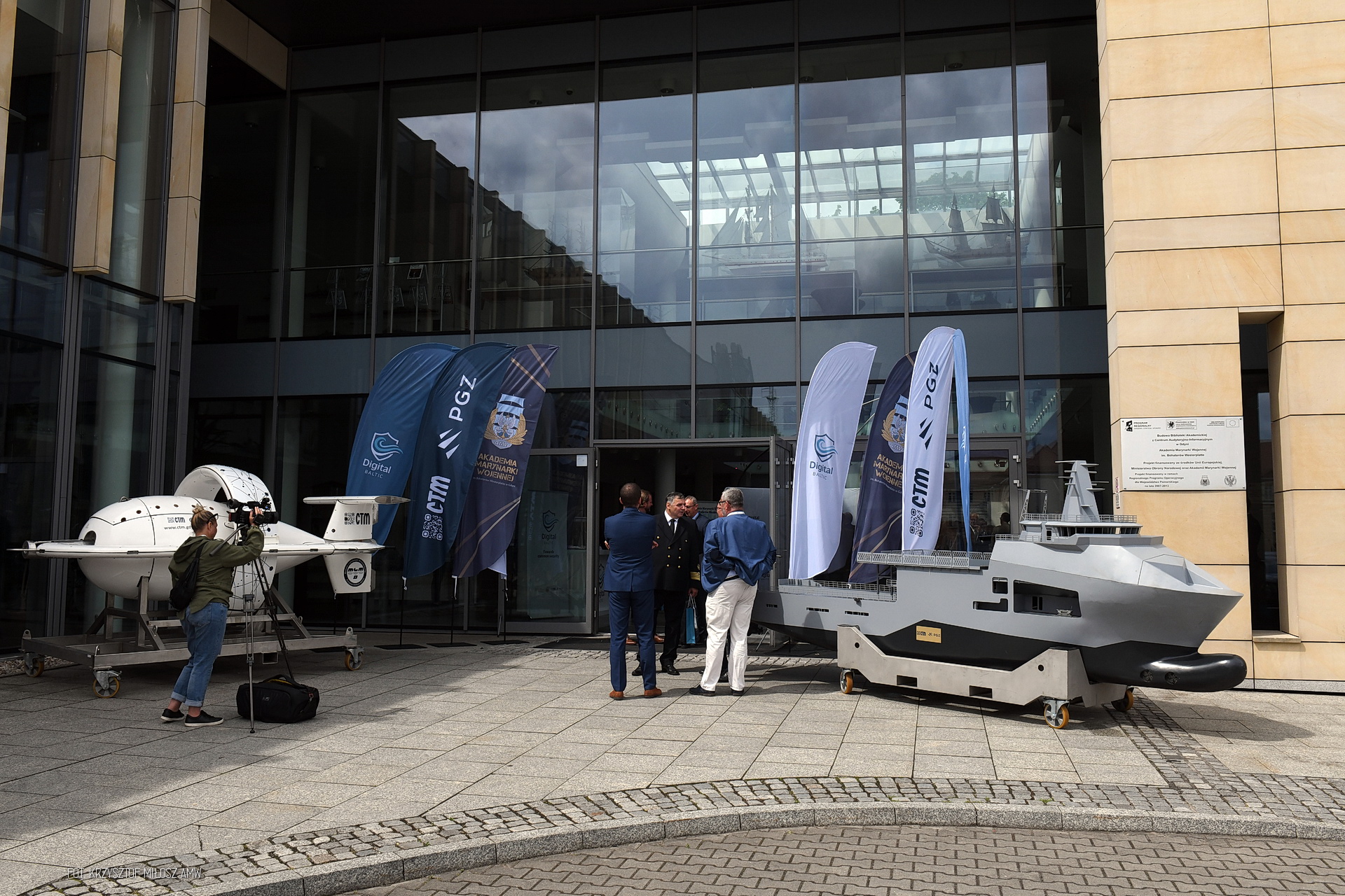 Modele drona podwodnego i okrętu przed wejściem na konferencję Digital Baltic — flagi PGZ, CTM i Akademii MW