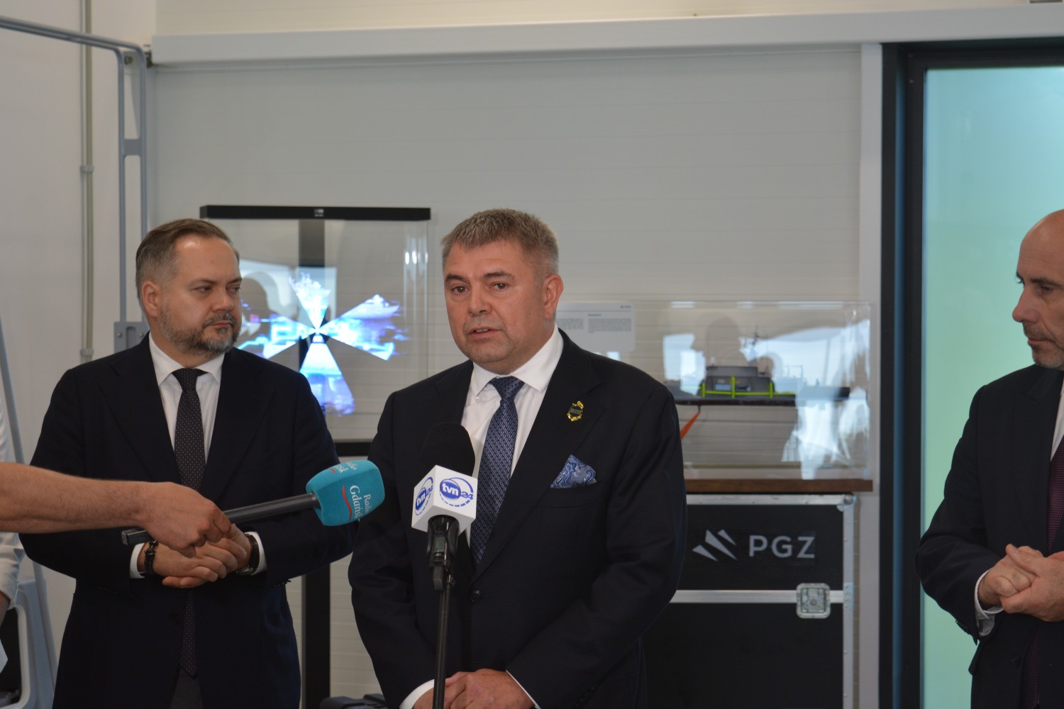 Przemówienie podczas konferencji prasowej otwarcia CEM — mikrofony Radio Gdańsk i TVN24, w tle model okrętu na skrzyni PGZ