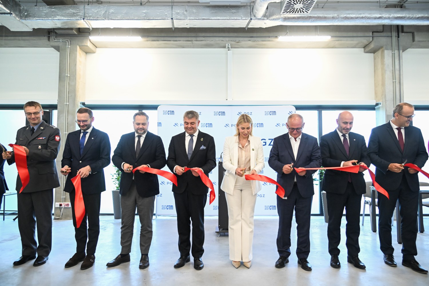Ośmiu uczestników ceremonii przecina czerwoną wstęgę na tle ścianki z logotypami CTM i PGZ — w tym przedstawiciel Marynarki Wojennej