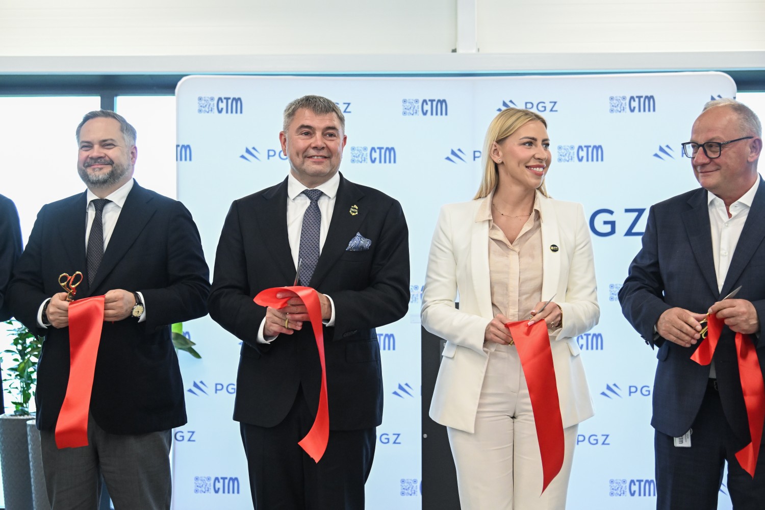 Czterech przedstawicieli po przecięciu wstęgi podczas otwarcia Centrum Elektroniki Militarnej — ścianka promocyjna CTM i PGZ w tle