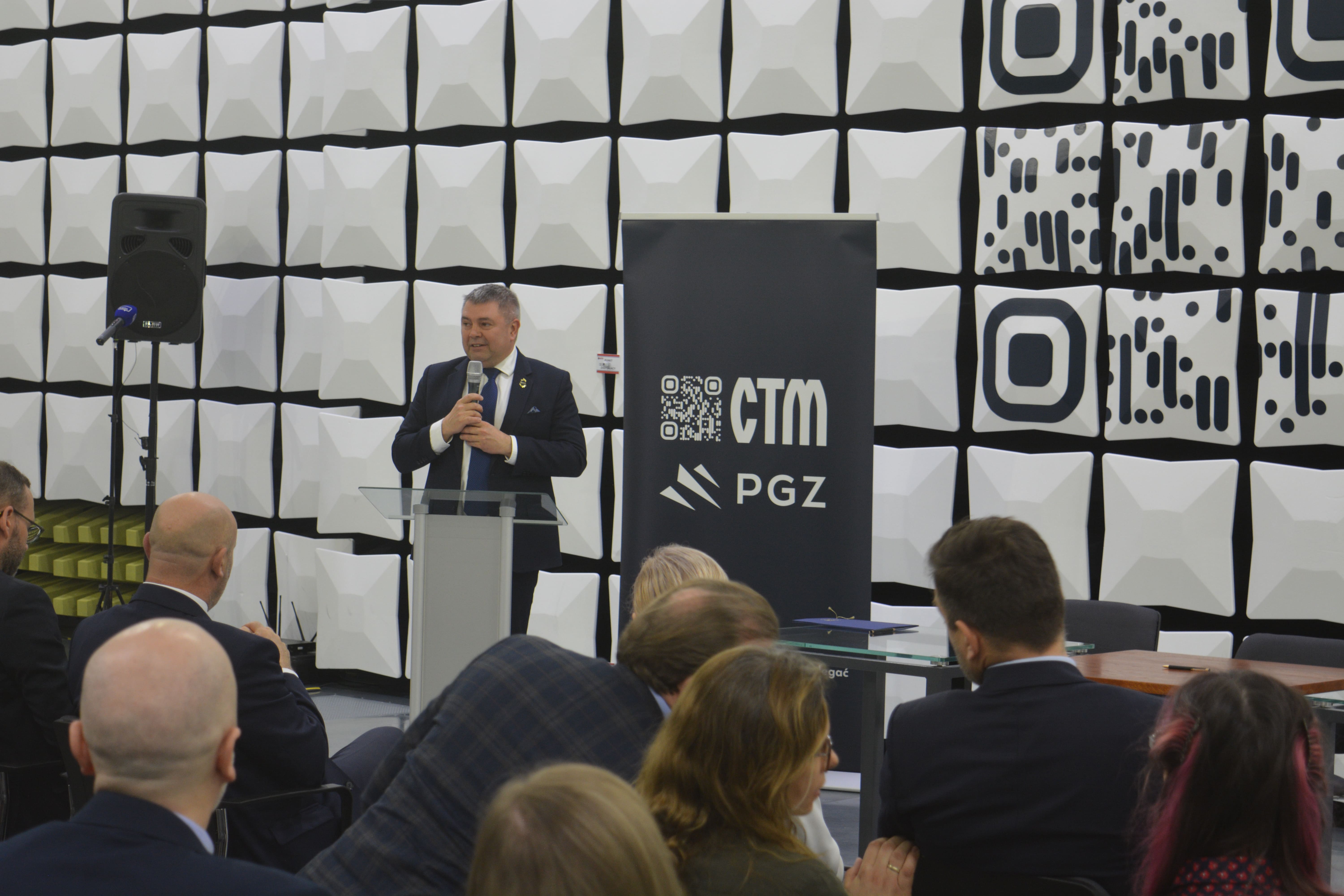 Marcin Wiśniewski przemawia przy mównicy w komorze bezechowej CTM — obok baner z logo CTM i PGZ