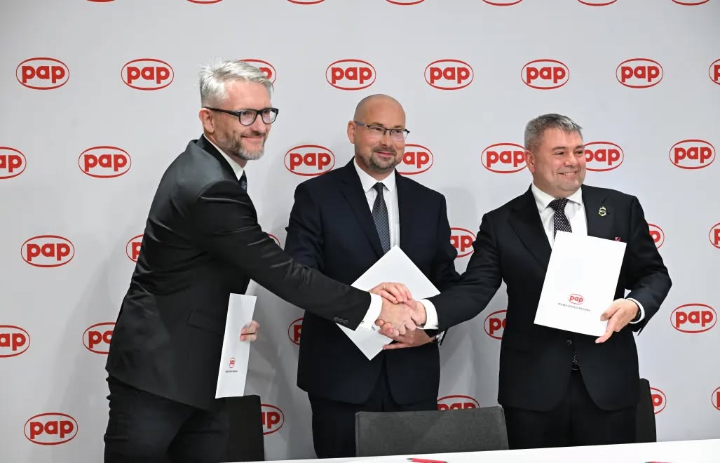 Trzej przedstawiciele CTM, PAP i GPW DAI podają sobie ręce z białymi teczkami na tle ścianki z logotypami PAP