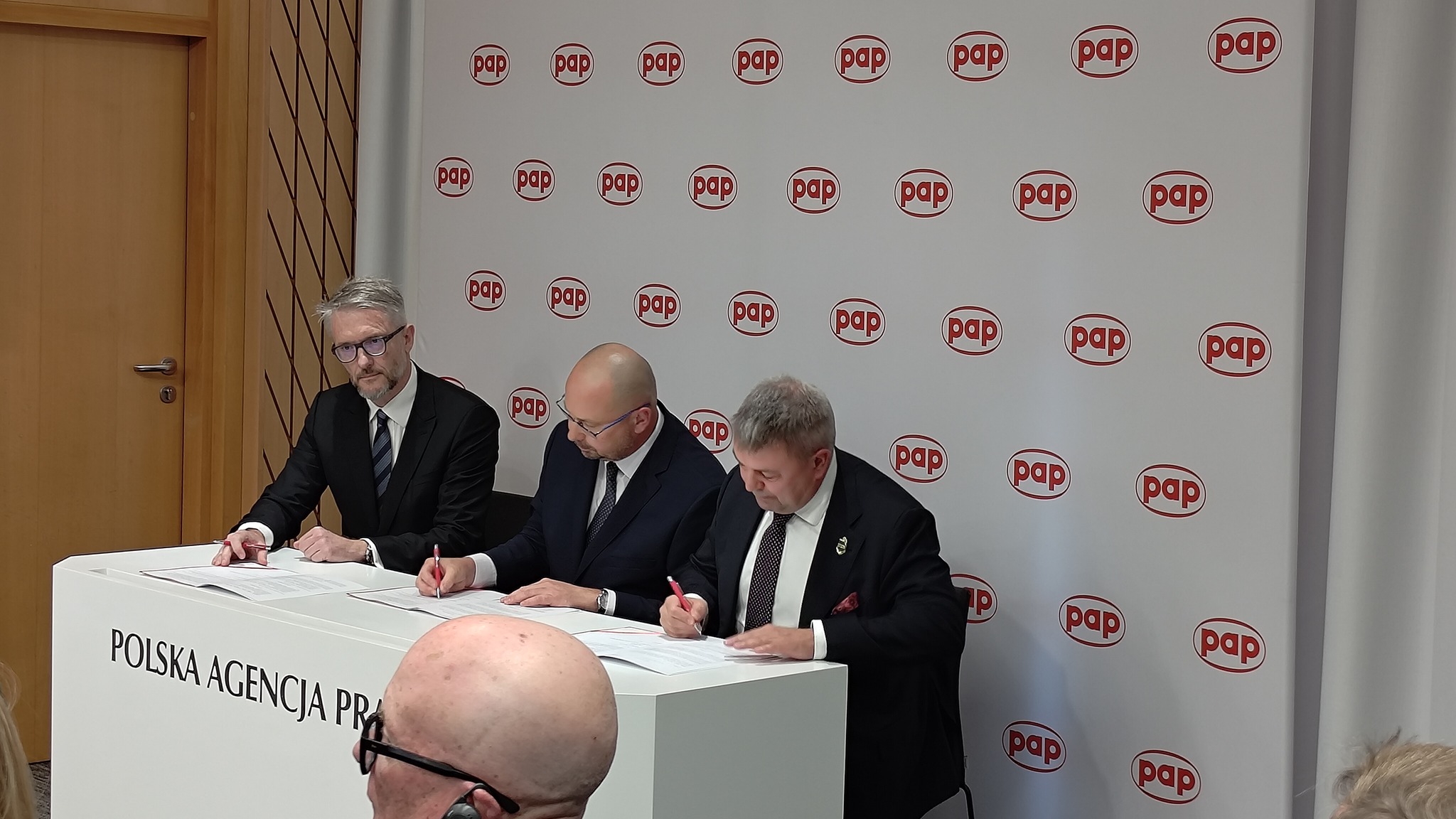 Podpisanie listu intencyjnego — trzech mężczyzn przy stole z napisem Polska Agencja Prasowa na tle ścianki z logo PAP