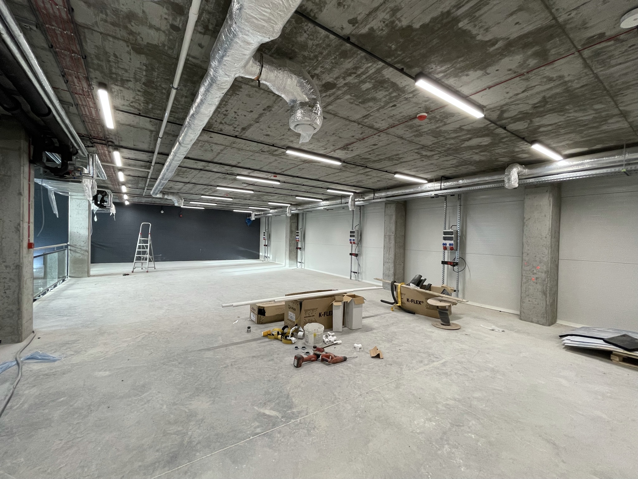 Sala laboratoryjna w trakcie wykończenia — instalacje wentylacyjne pod sufitem, oświetlenie LED i materiały budowlane na posadzce