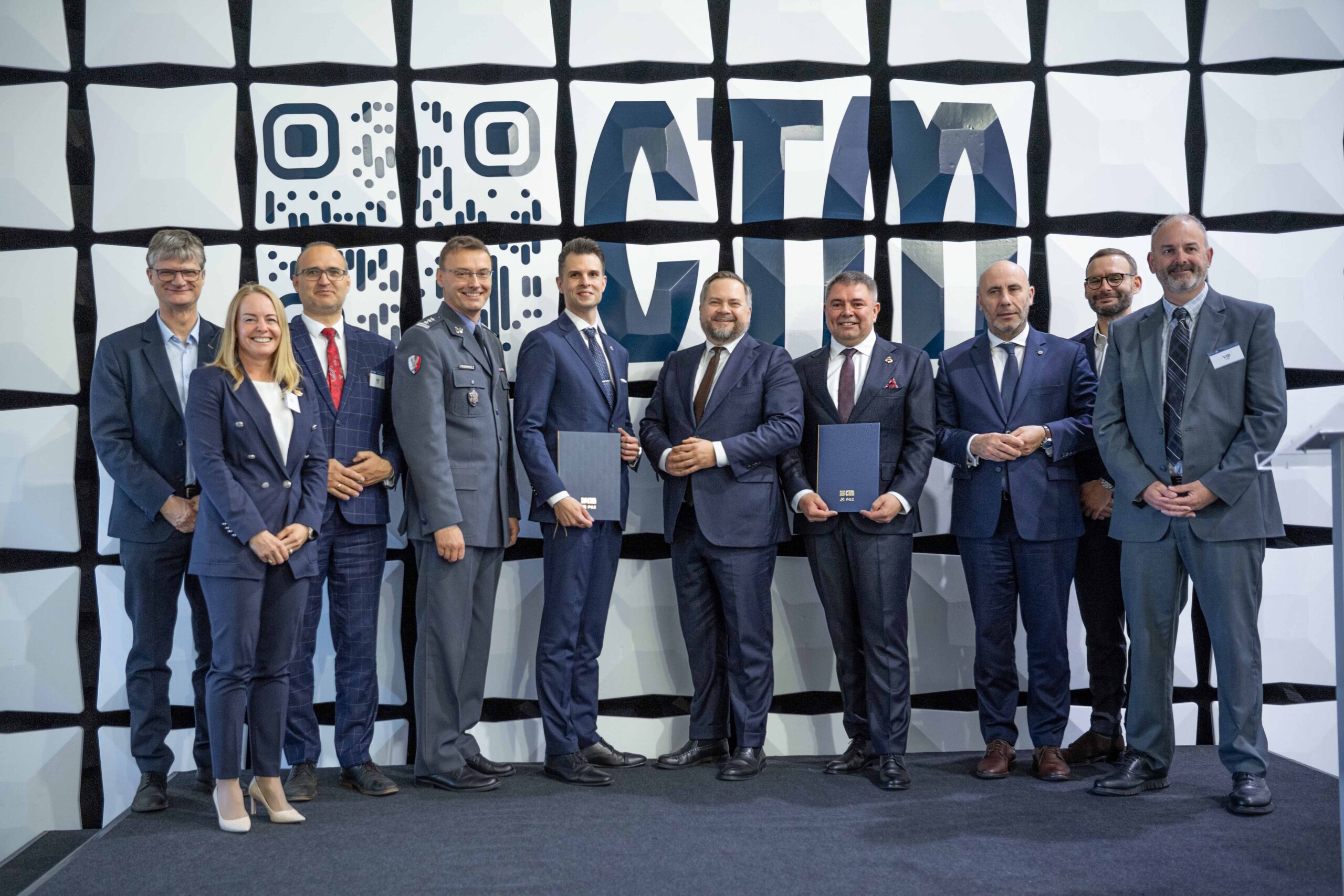 Grupowe zdjęcie uczestników uroczystości — dwóch mężczyzn z granatowymi teczkami CTM po podpisaniu porozumienia z WZE