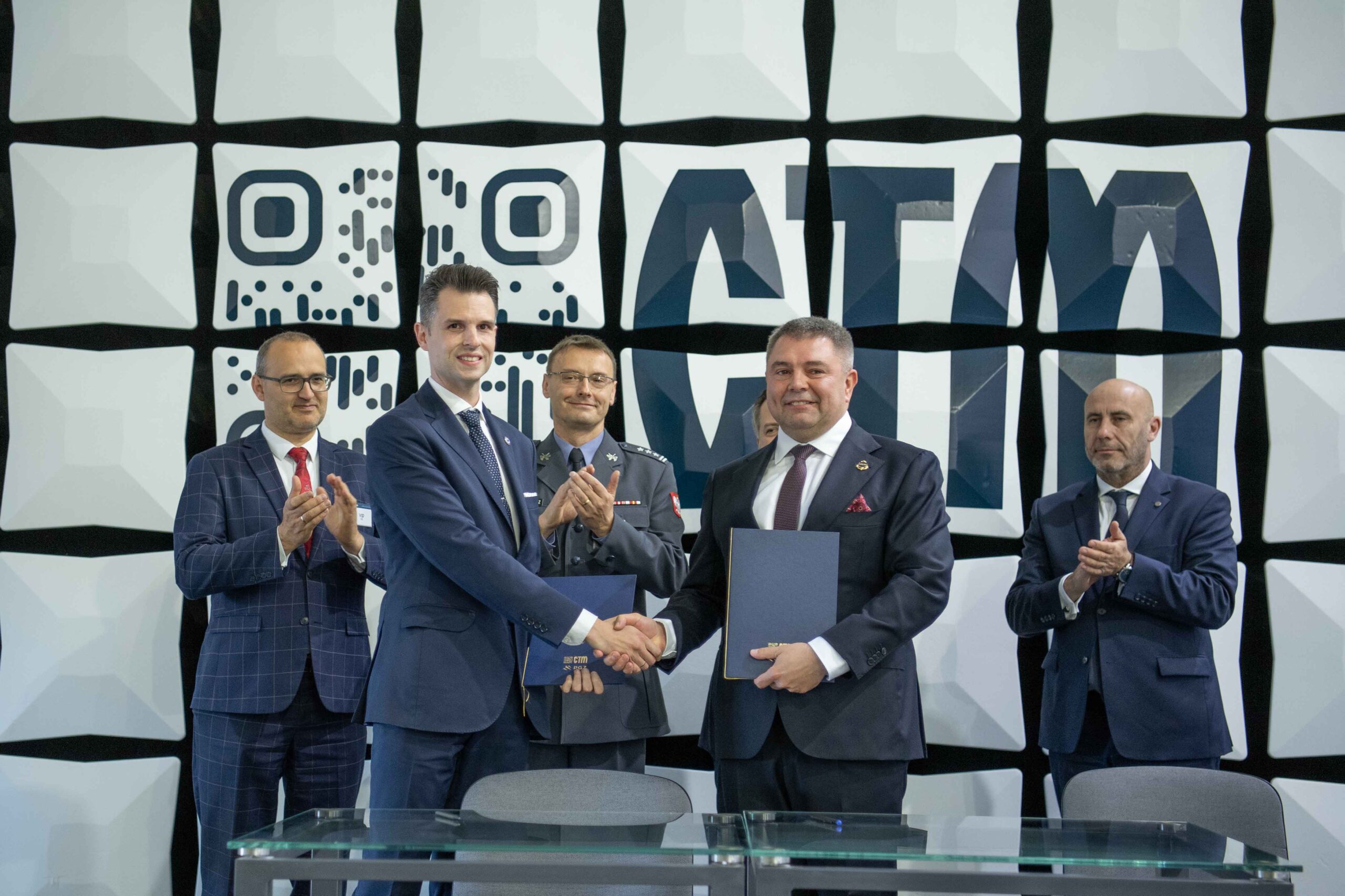 Uścisk dłoni po podpisaniu listu intencyjnego CTM i WZE — granatowe teczki z logo CTM, klaszczący świadkowie na tle ściany z logo CTM