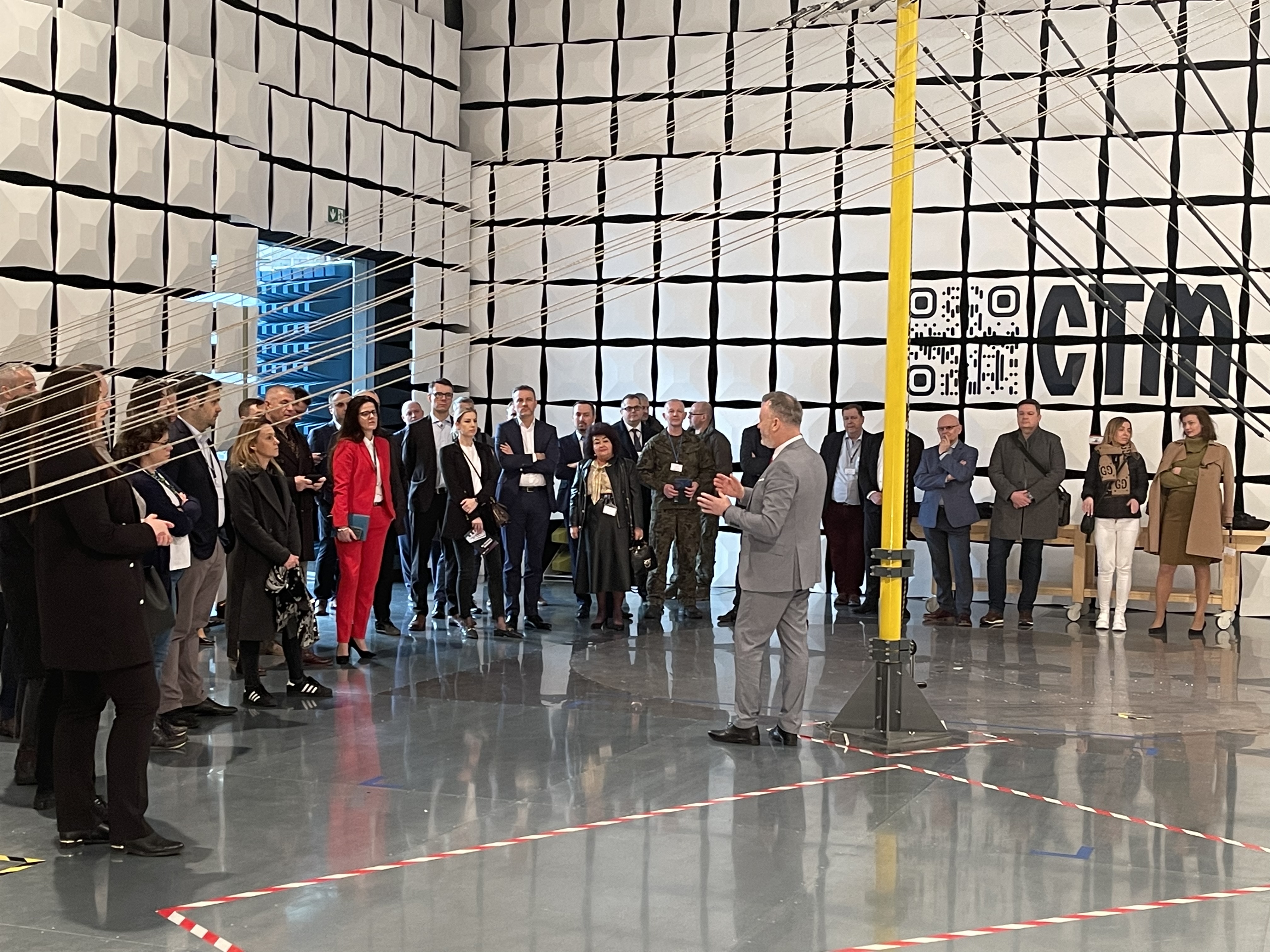 Zwiedzanie komory bezechowej laboratorium EMC LabNet — grupa gości na tle logo CTM i kodu QR